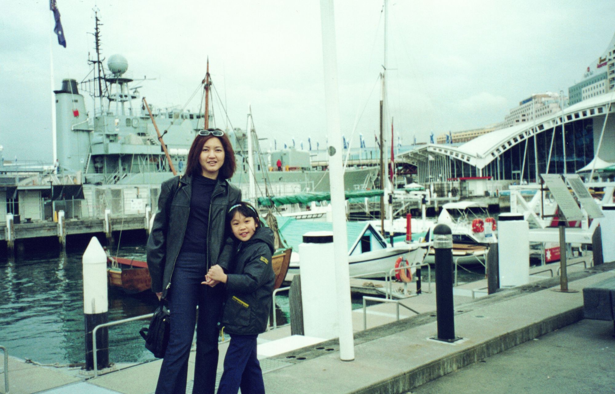 My mother and me at a marina, a grey naval ship behind