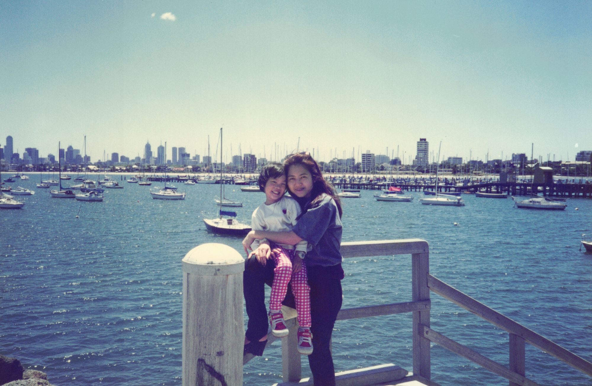 My mother holding me at a harbour rail, a city skyline across the water