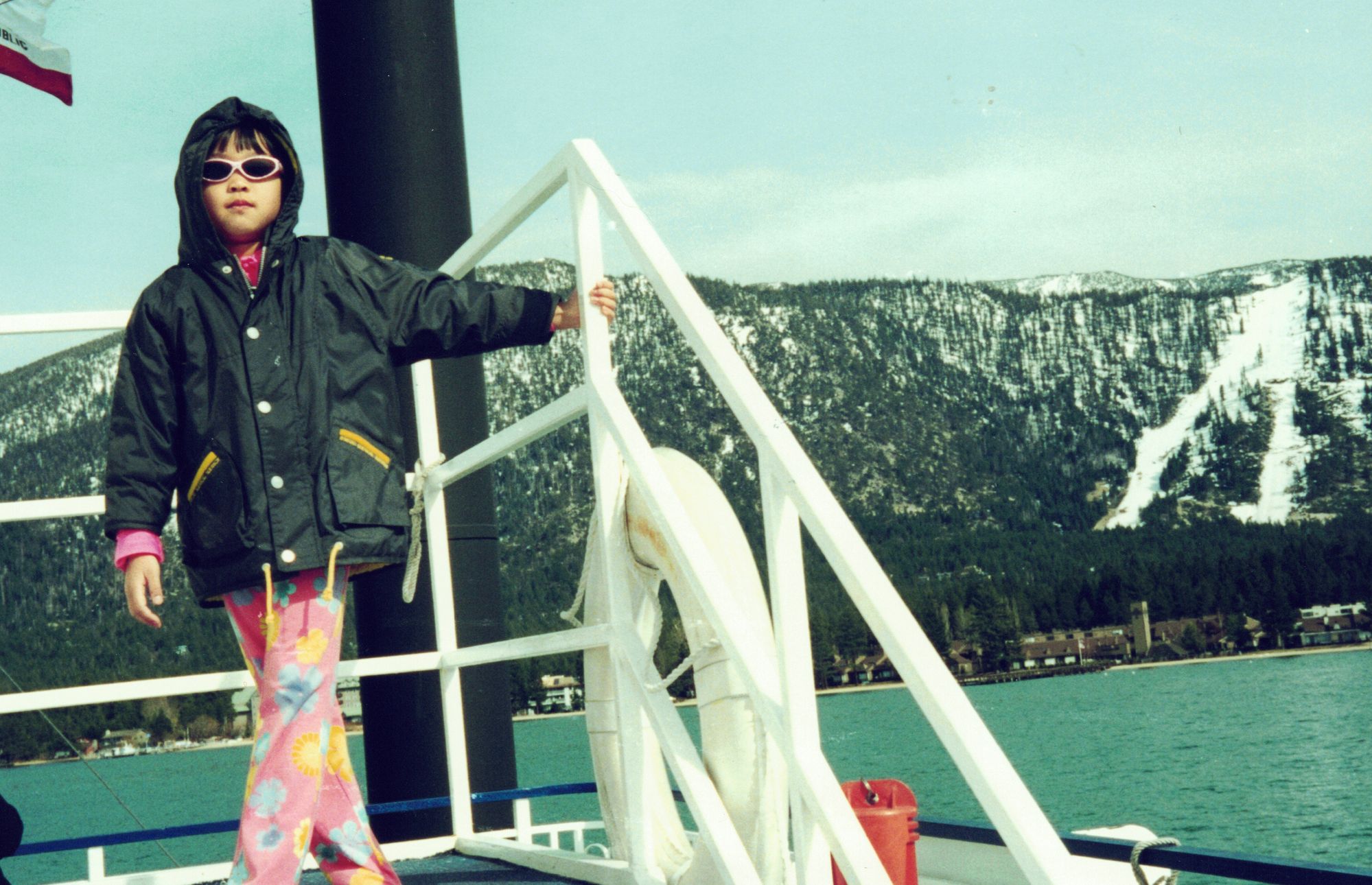 Me in sunglasses on the white deck of a boat, snowy mountains across the water