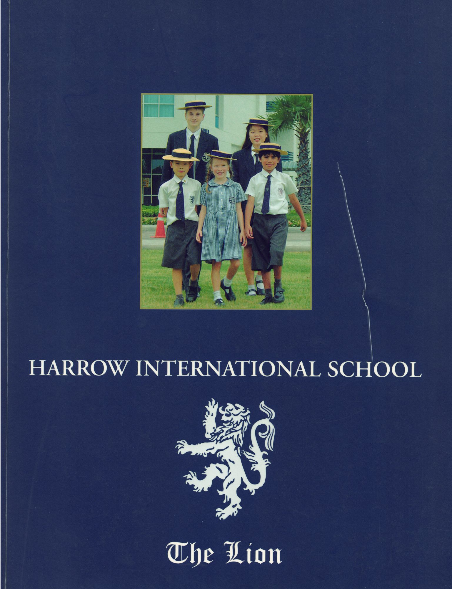 The Lion, the 2003–2004 Harrow International School yearbook — a navy cover with the school crest and a photograph of five pupils in boaters