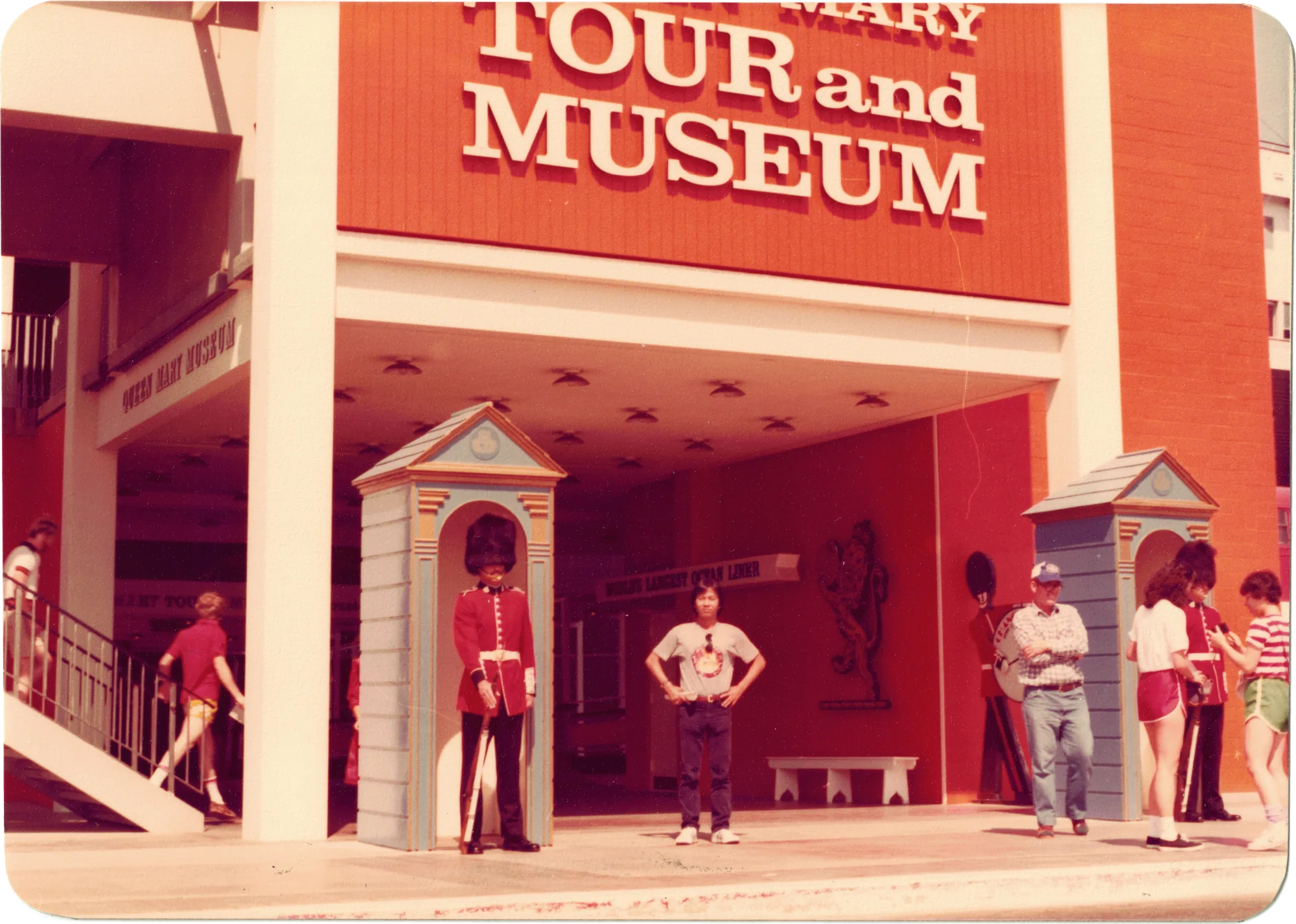 My father in a T-shirt and jeans in front of a red Tour and Museum entrance, flanked by two costumed guards in sentry boxes — a rounded-corner print