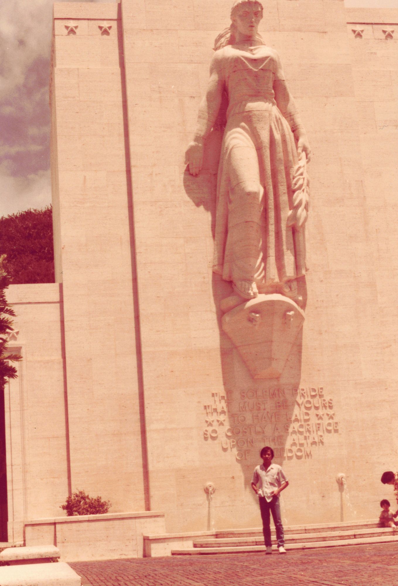 My father standing small at the foot of a tall stone monument with a robed figure carved above him