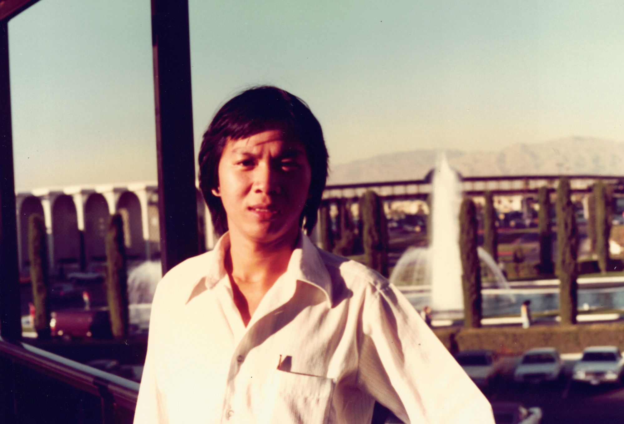 A close portrait of my father in a white shirt, an arcaded building and a fountain behind him