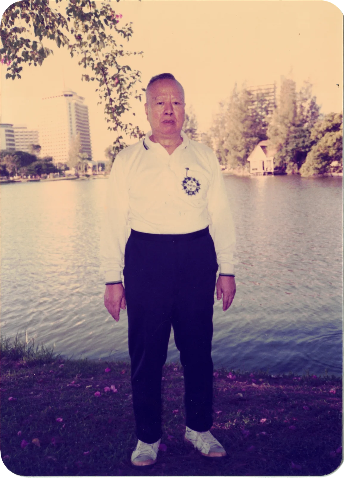 My grandfather in a white shirt standing on a lakeside lawn, tall buildings across the water — a rounded-corner print